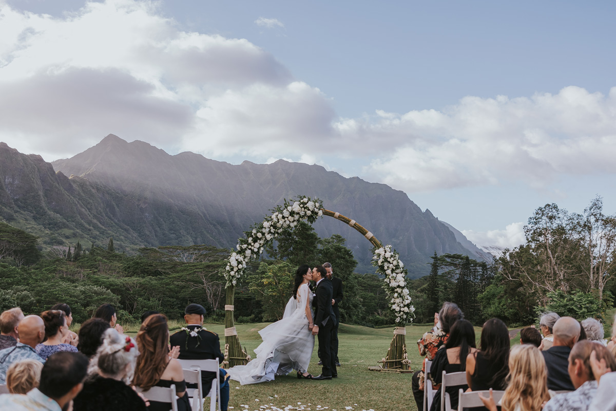  a couple kssing in front of arch at koolau ballrooms with koolau mountain range in the back